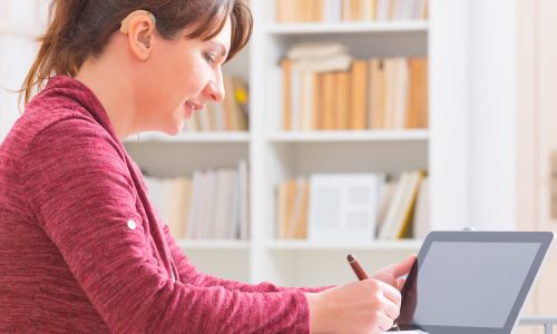 Photo of a woman with a hearing aid writing in a note book.