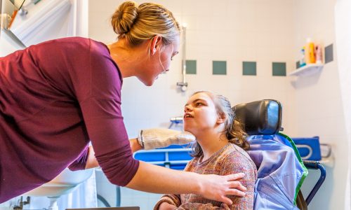 Woman with her hand on the shoulder of a girl with disability talking to her.