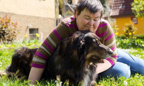 Woman with intellectual disability lying on the grass with a dog.