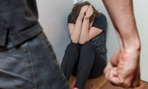 Photo of a woman crunched down in a corner with a man standing over her