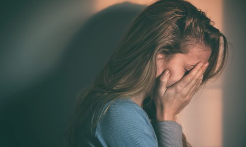 Photo of a woman standing in a dark room holding her head in her hands.