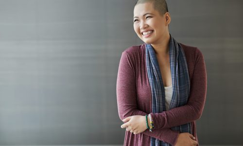 Photo of an asian woman with a bald head leaning against a wall.