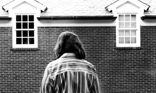 a back and white image of a woman looking down in front of a dark building.