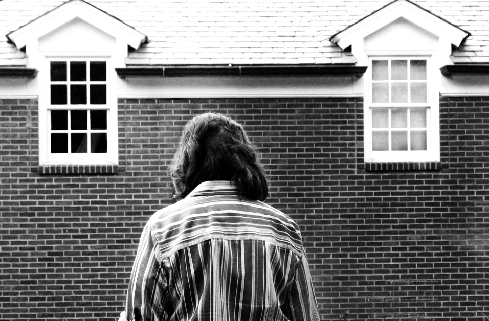 a back and white image of a woman looking down in front of a dark building.