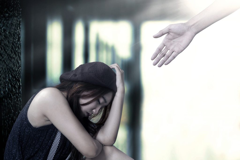 Photo of woman sitting down looking sad with someone reaching out their hand to help.