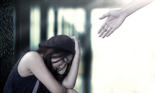 Photo of woman sitting down looking sad with someone reaching out their hand to help.