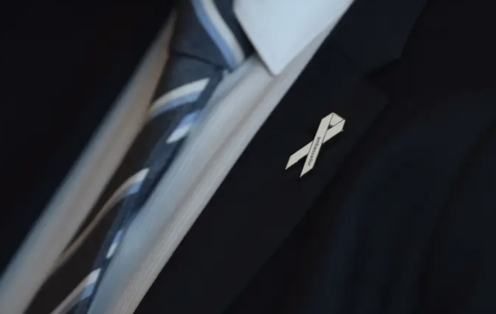 Photo of a white ribbon pinned to a mans suit jacket.