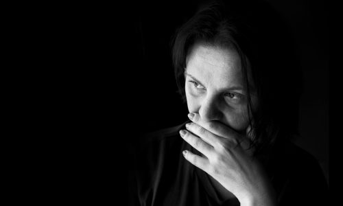 Greyscale photo of a woman with her hand to her mouth sitting in the dark.