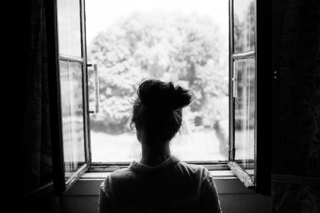 Greyscale photo of a woman looking out of an open window.