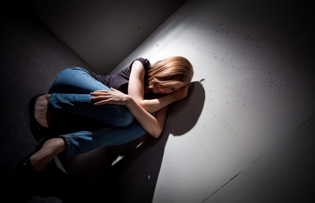 Photo of woman sitting down in a dark corner.