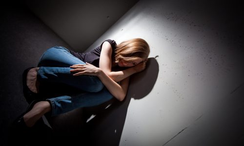 Photo of woman sitting down in a dark corner.