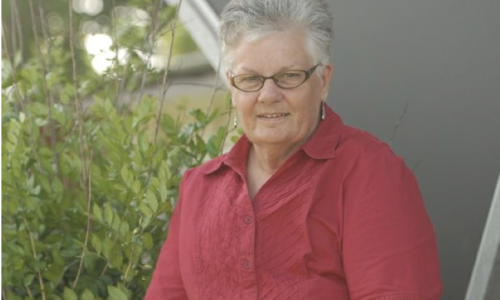 Photo of Jude Marshall, wearing a red shirt and glasses with short grey light hair.