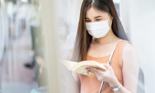 Young Asian woman passenger wearing surgical mask and reading the book in subway train when traveling in big city at Covid19 outbreak, Infection and Pandemic concept