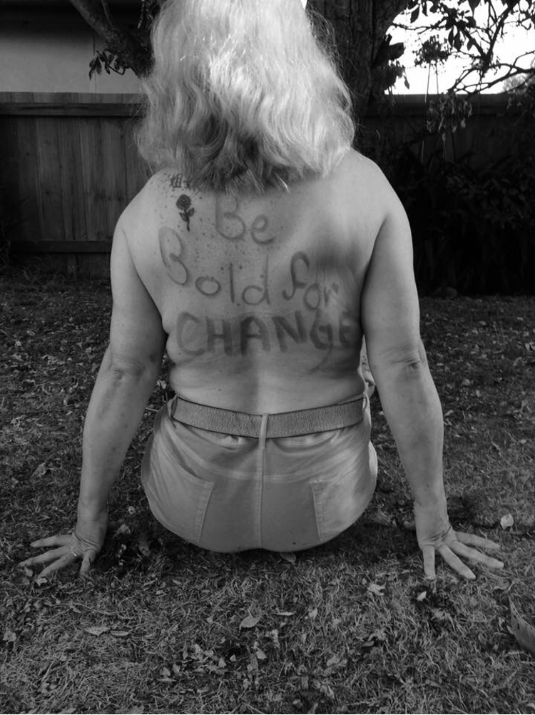 Photo of Tammy Milne, sitting on grass, facing away from the camera with the words "Be Bold for CHANGE" written in texter on her back.