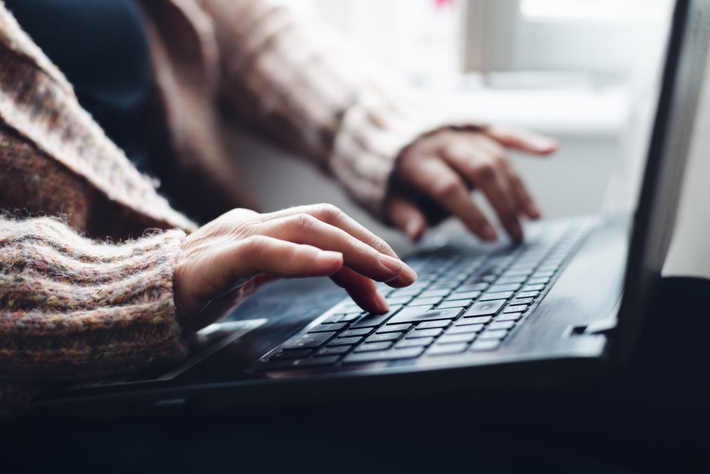 A woman working on a laptop, the photo is cropped so you can only see her hands and the laptop.