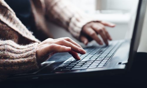 A woman working on a laptop, the photo is cropped so you can only see her hands and the laptop.