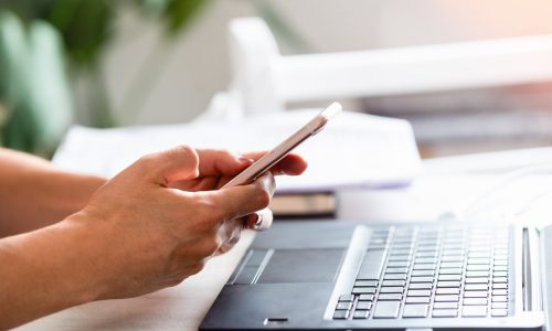 Woman watching cell phone while working on computer.