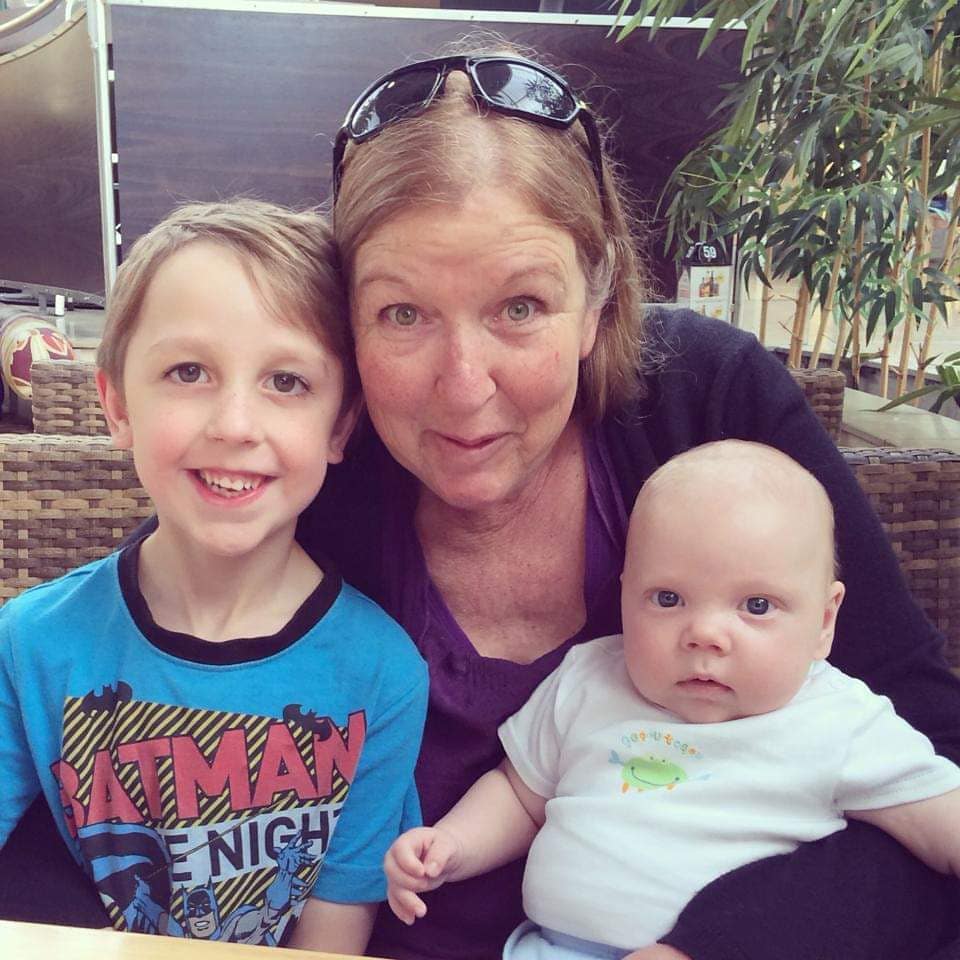 My beautiful mum, and her grandbabies
A middle-aged white woman sits between two young children, cuddling them and smiling. They are all facing the camera.