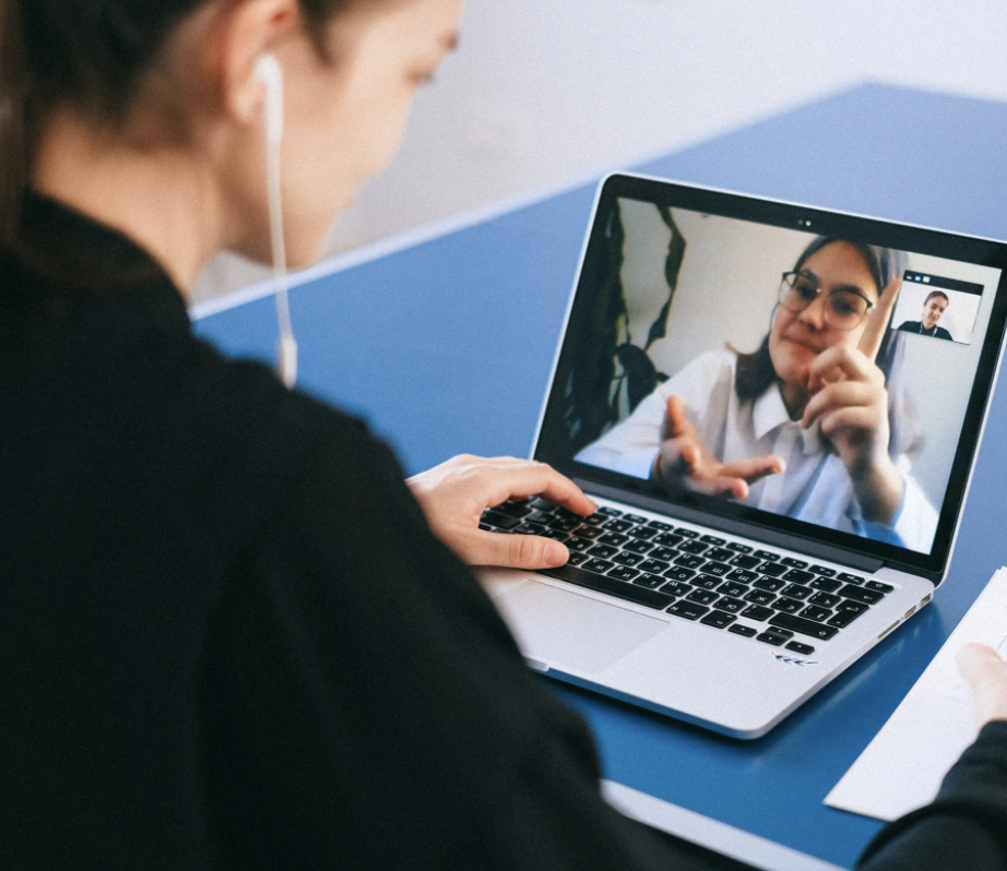 A young woman using a laptop with headphones in. On the screen is another young woman talking in Auslan.