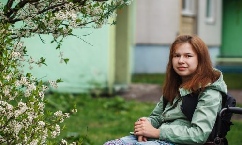 Photo of a young girlw ith brown hair sitting in a wheelchair in the garden under a blossoming tree