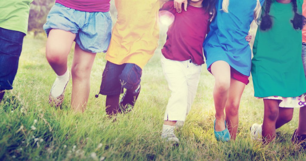 photo of a group of children linking arms and walking in a line through a field.