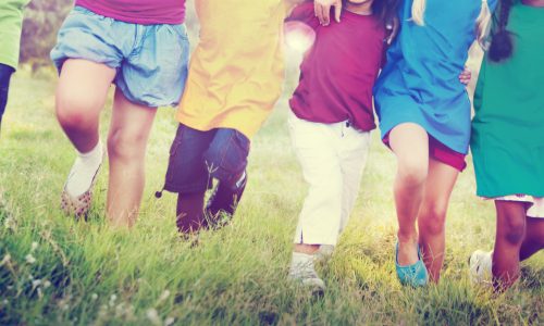 photo of a group of children linking arms and walking in a line through a field.