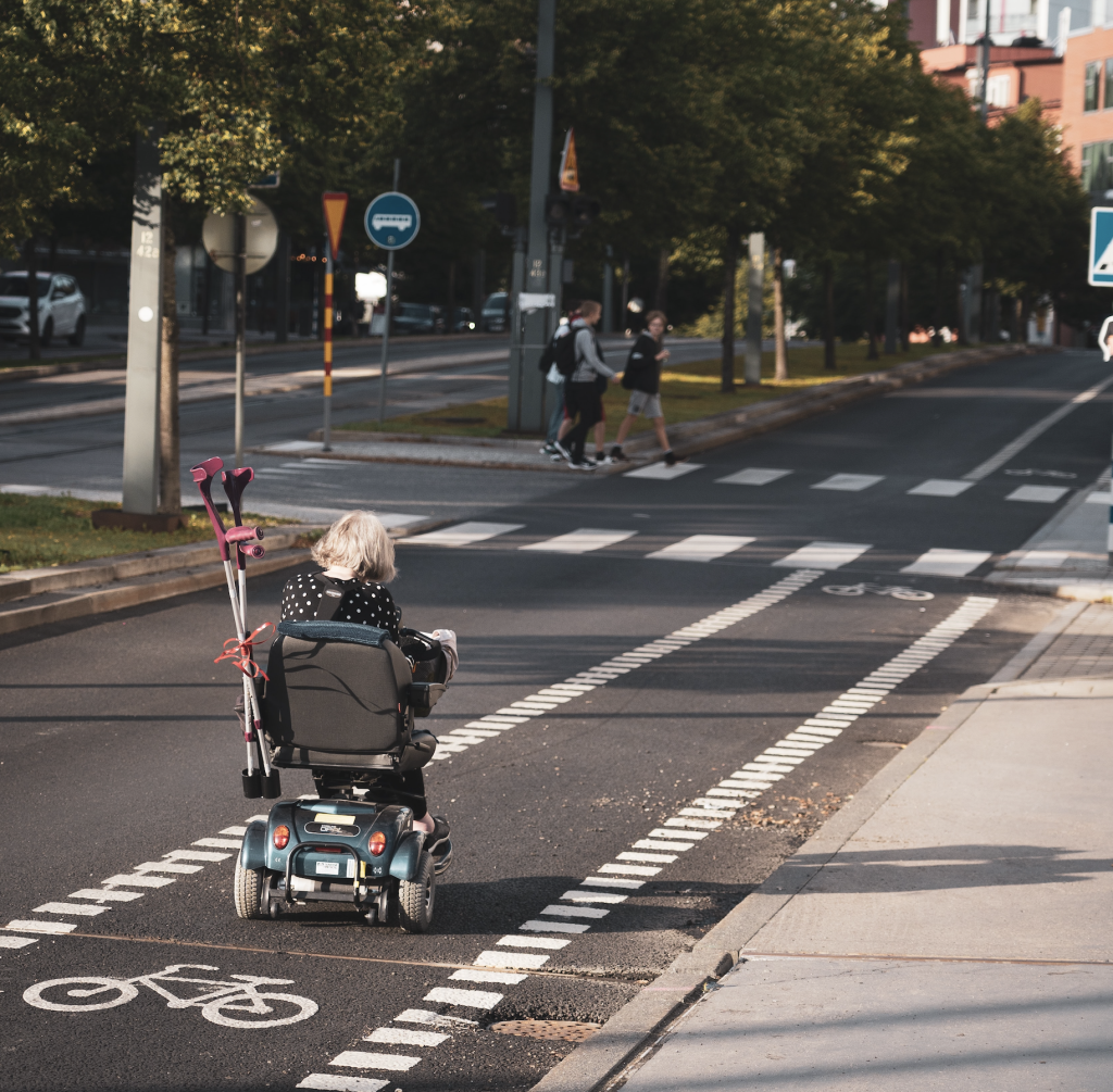 Photo of a person using a motorised wheelchair moving along a bike lane on a road