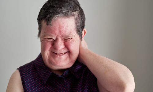 Photo of a woman with disability, laughing with her hand up behind her head.