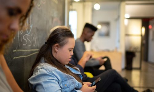 A woman with down syndrome sitting on a bench looking down at a smart phone.