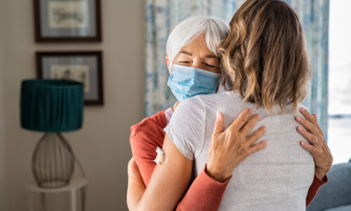 Senior woman wearing face mask hugging immunized daughter after covid-19 vaccination shot. Elderly grandmother hugging adult granddaughter after covid vaccine jab. Immunity and end of covid19 pandemic