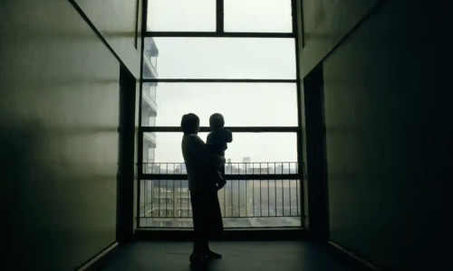 Photo of a woman standing in a dark long corridor holding a small child.