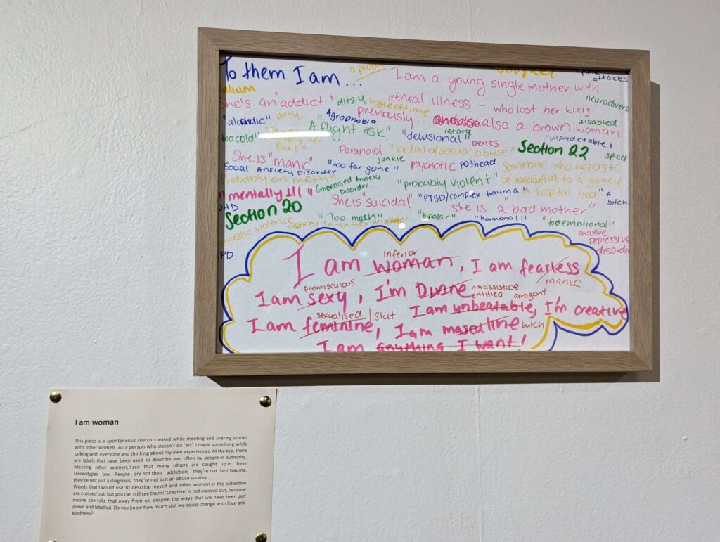 A framed written artwork on a gallery wall, showing labels given to women with mental health conditions