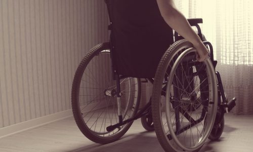 Photo of a woman in a wheelchair looking out a window.