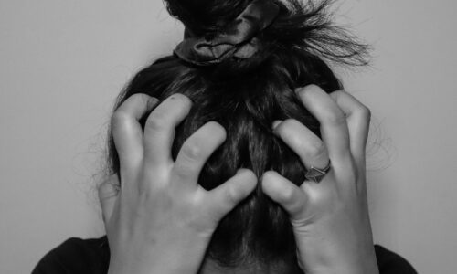 a stock image of a woman with her hair tied up in a messy bun and she is scrunching her hair on her head. The photo is in black and white.