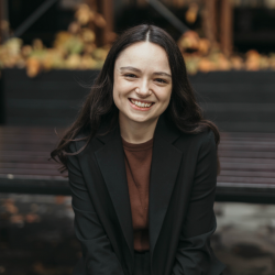 Photo of Sophie Cusworth, WWDA CEO, Sophie has long darl brown hair, fair skin and is wearing a brown top and black blazer. She is sitting smiling in a park.